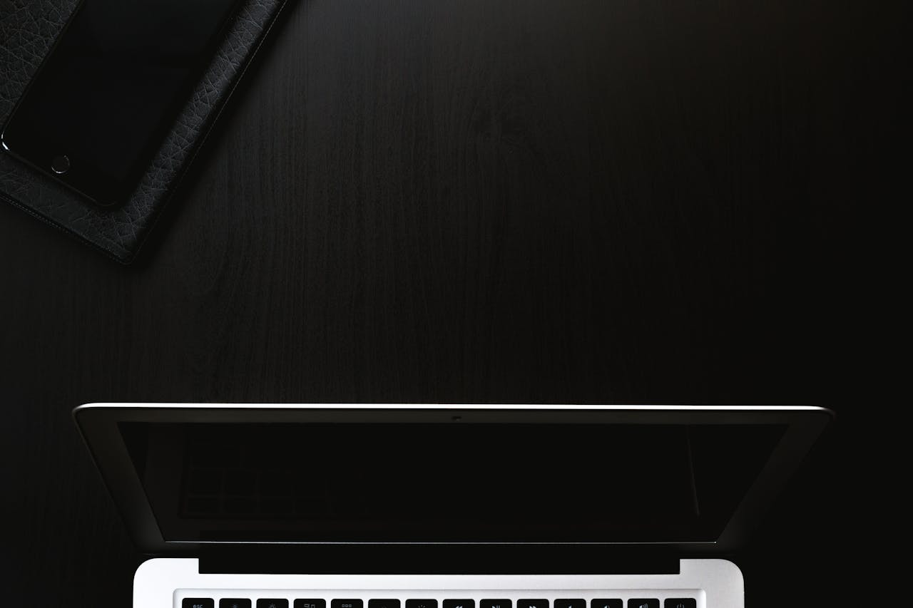 A sleek and minimalist workspace featuring a laptop and smartphone on a dark surface.